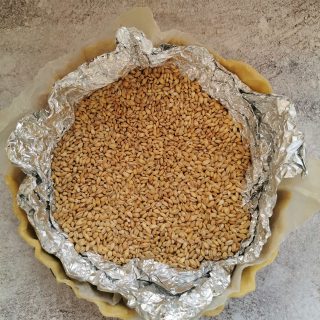 a pie crust filled with pearl barley ready to be blind baked