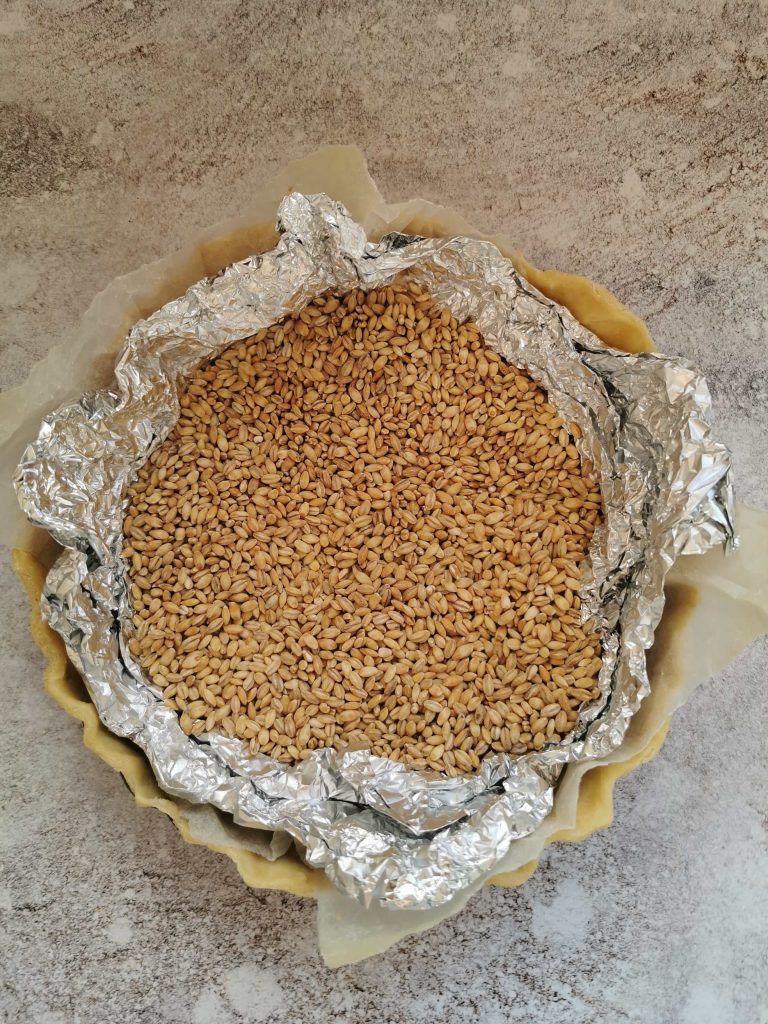 a pie crust filled with pearl barley ready to be blind baked.