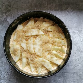 An unbaked cake topped with sliced apple and sprinkled with brown sugar