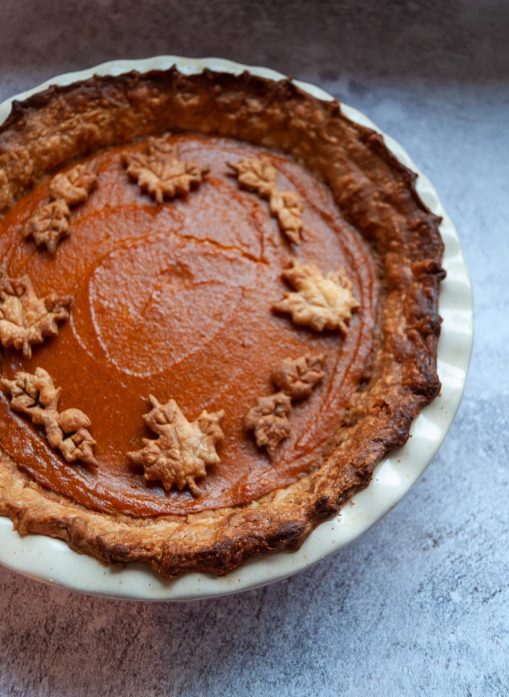 A pumpkin pie decorated with Autumn pastry leaves on a white and grey background