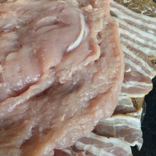 A butterflied turkey breast lying on rashers of bacon to make a rolled turkey breast 