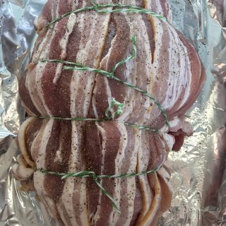 A rolled turkey breast wrapped in bacon and tied with string ready for the oven