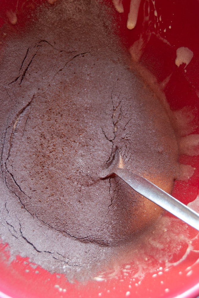 Cocoa powder and flour being folded into eggs and sugar