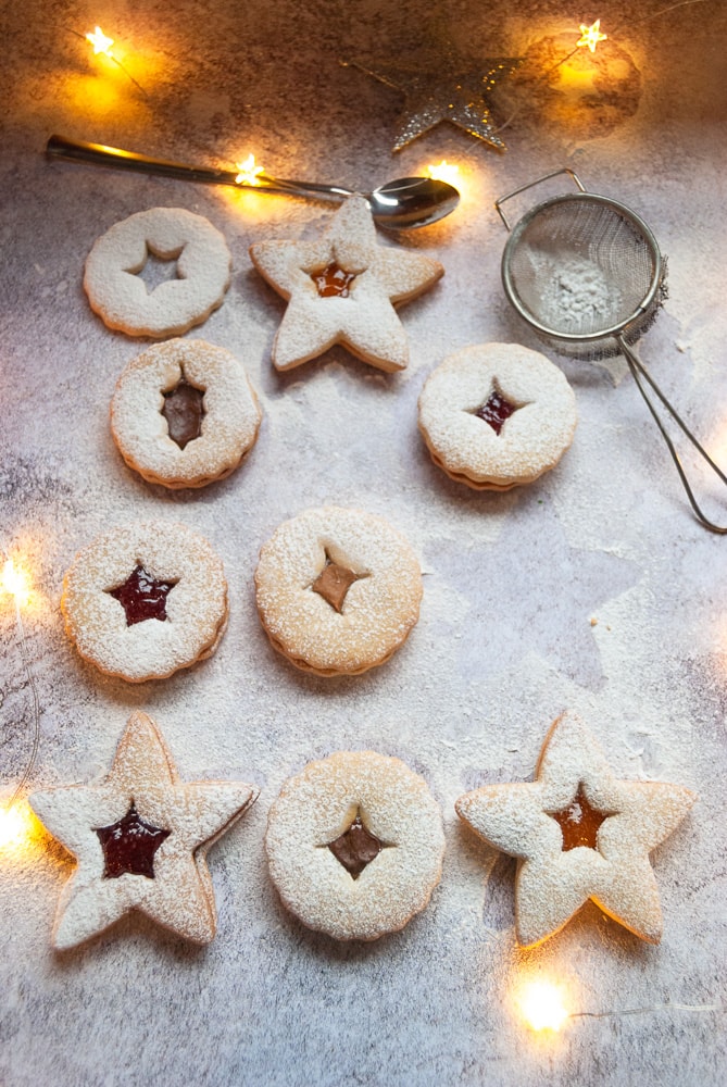 Jam filled Linzer cookies dusted with icing sugar on a white and grey background.