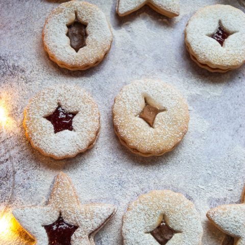 Linzer cookies filled with jam and Nutella and dusted with icing sugar on a white and grey background.