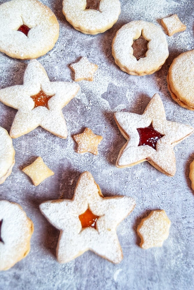 Christmas linzer cookies filled with jam and dusted with icing sugar on a grey and white background