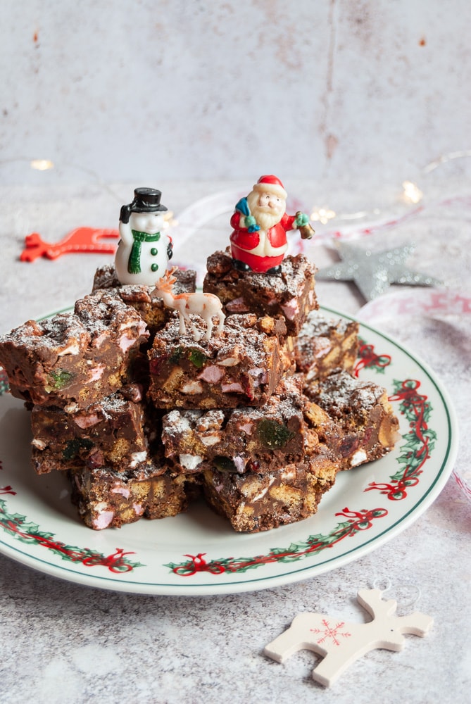 rocky road bars piled up on a Christmas plate with santa, snowman and reindeer figures. 