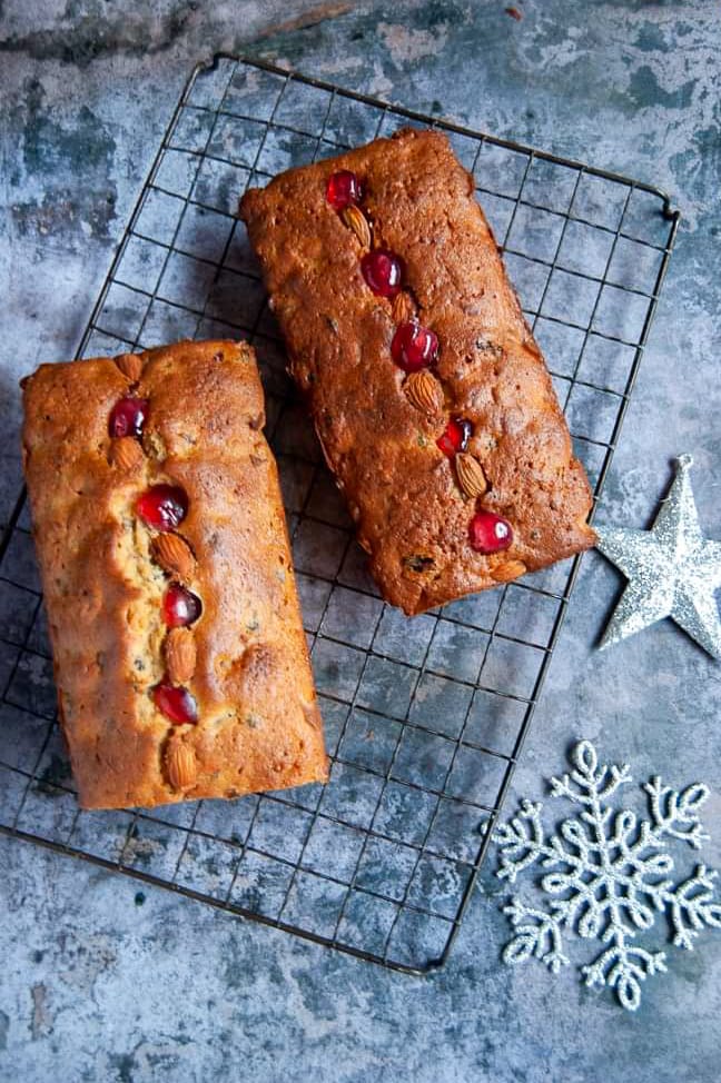 Two mincemeat loaf cakes on a black wire rack studded with glace cherries and almonds