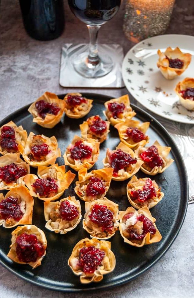 Mini turkey filo pies topped with cranberry sauce on a black plate