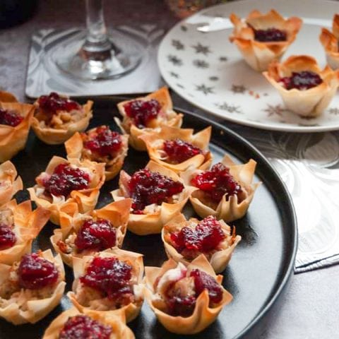 A black plate of turkey and cranberry filo pies with a glass of red wine in the background.