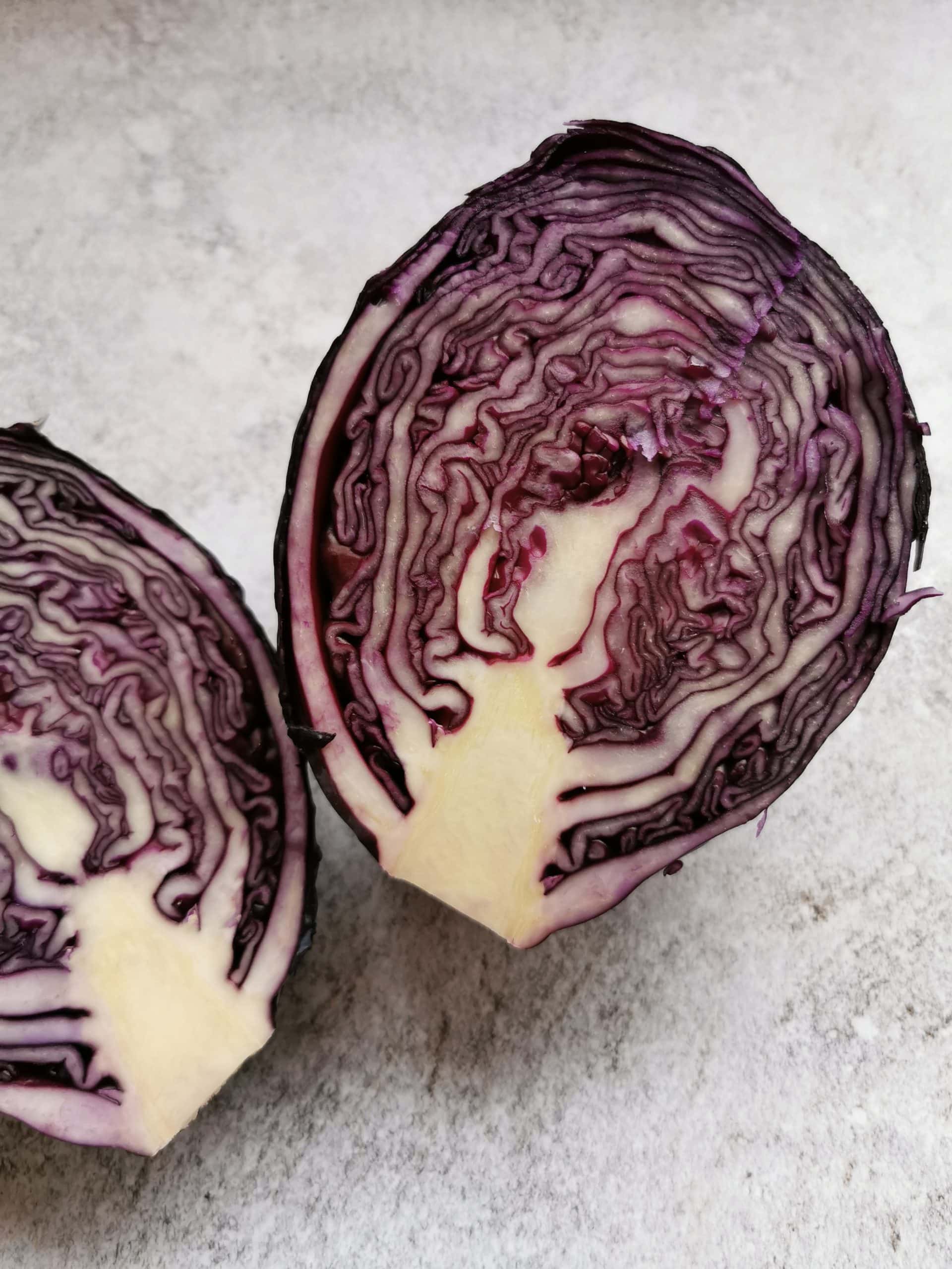 A red cabbage cut in half on a grey background. 