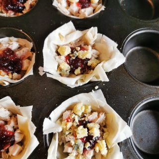 A muffin tin lined with filo pastry, turkey, stuffing, cranberry sauce and crumbled stilton
