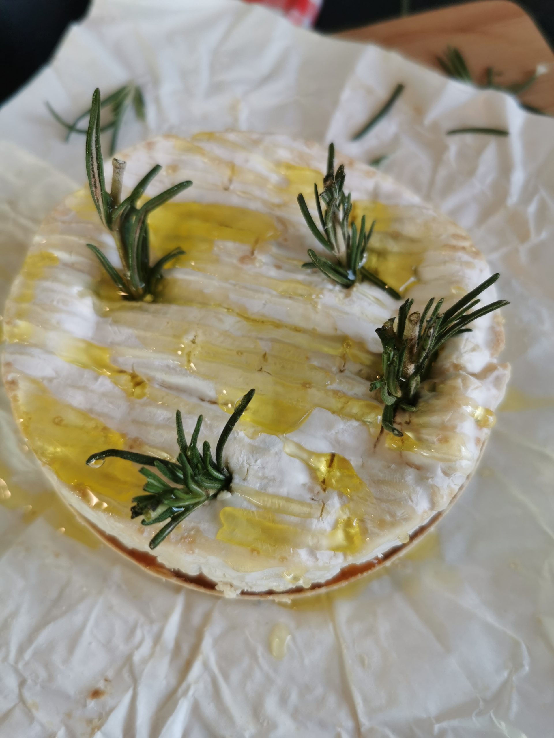 A whole Camembert cheese drizzled with olive oil and studded with fresh rosemary sprigs