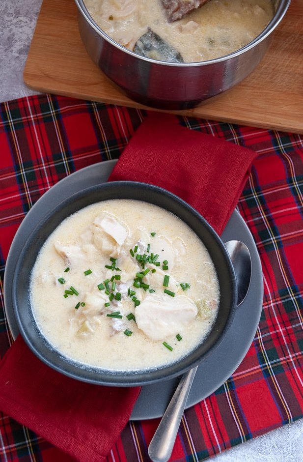 A bowl of Cullen Skink spinkled with fresh chives on a grey plate and red tartan tablecloth