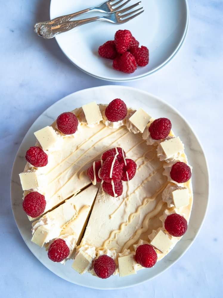 A white chocolate and raspberry cheesecake with a slice cut, ready to be served.