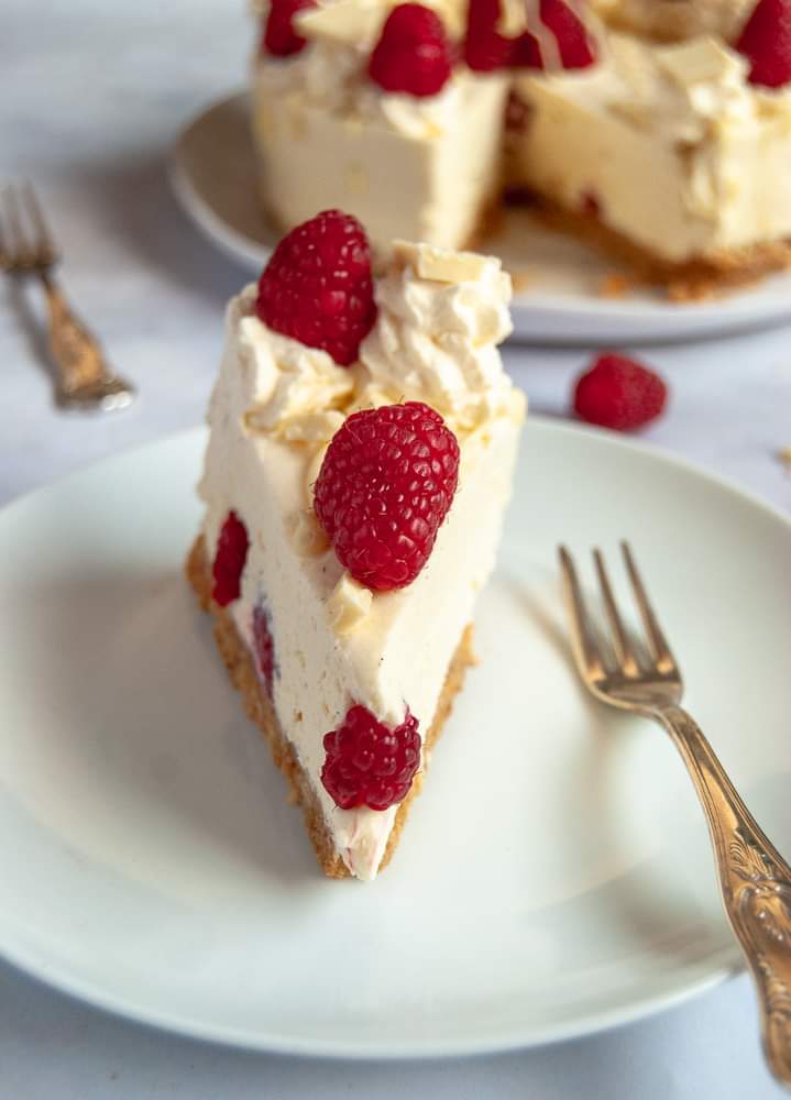 A slice of white chocolate and raspberry cheesecake on a white plate with a silver fork