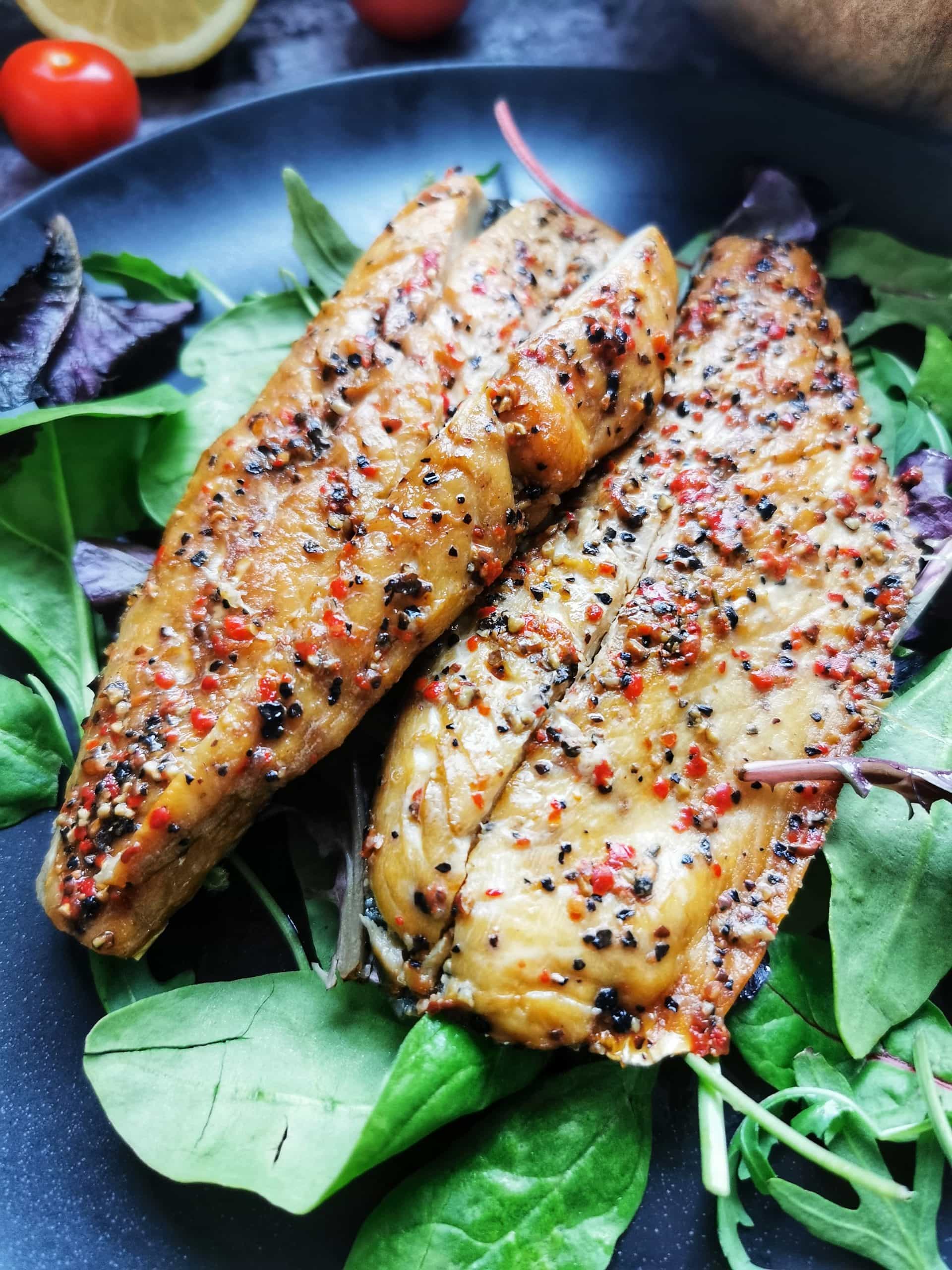 Two peppered mackerel fillets and salad leaves in a brown wooden bowl