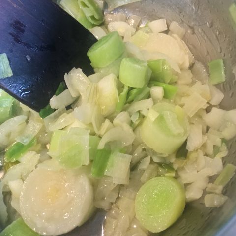 A pan of sauteed leeks and onion with a wooden spoon