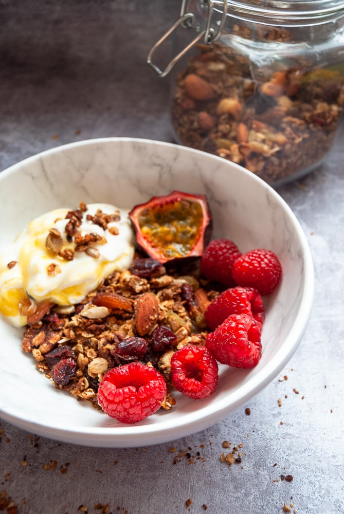 A close up picture of a bowl of Greek yogurt, raspberries, passion fruit and granola with nuts and seeds