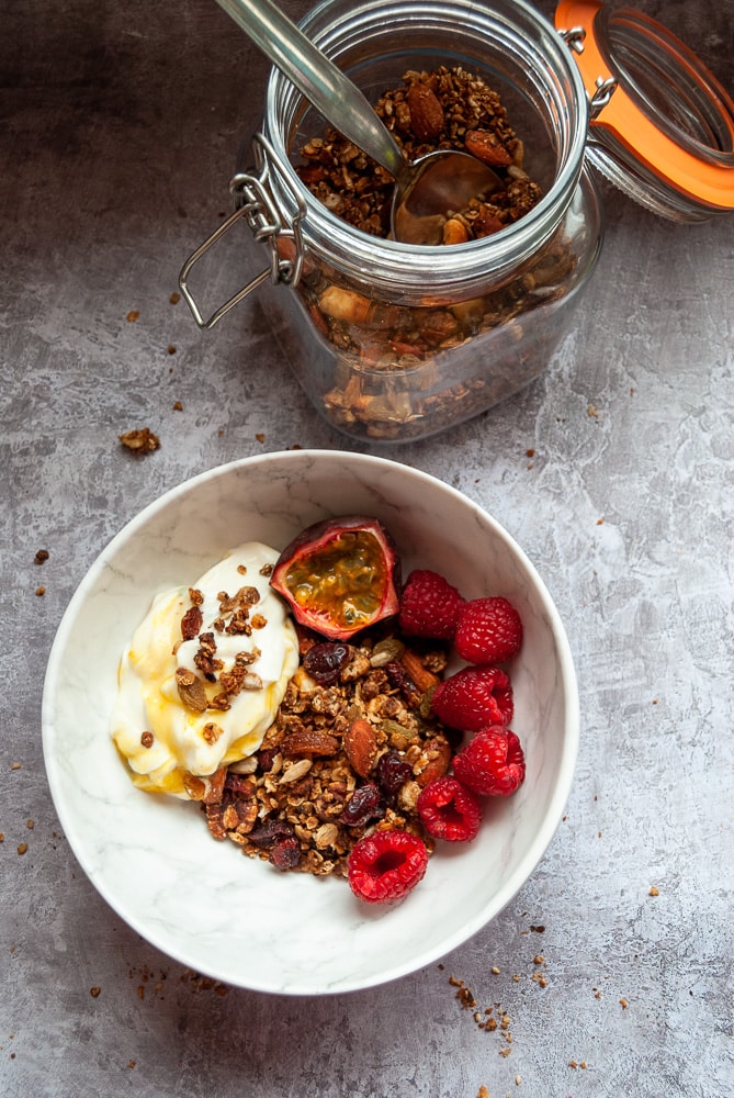 A bowl of granola with yoghurt, raspberries and a halved passion fruit. 