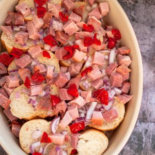 An oval casserole dish layered with baguette slices, diced red onion and red peppers