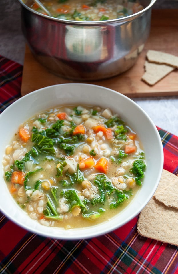 A bowl of scotch broth on a tartan tablecloth with oatcakes on the side.