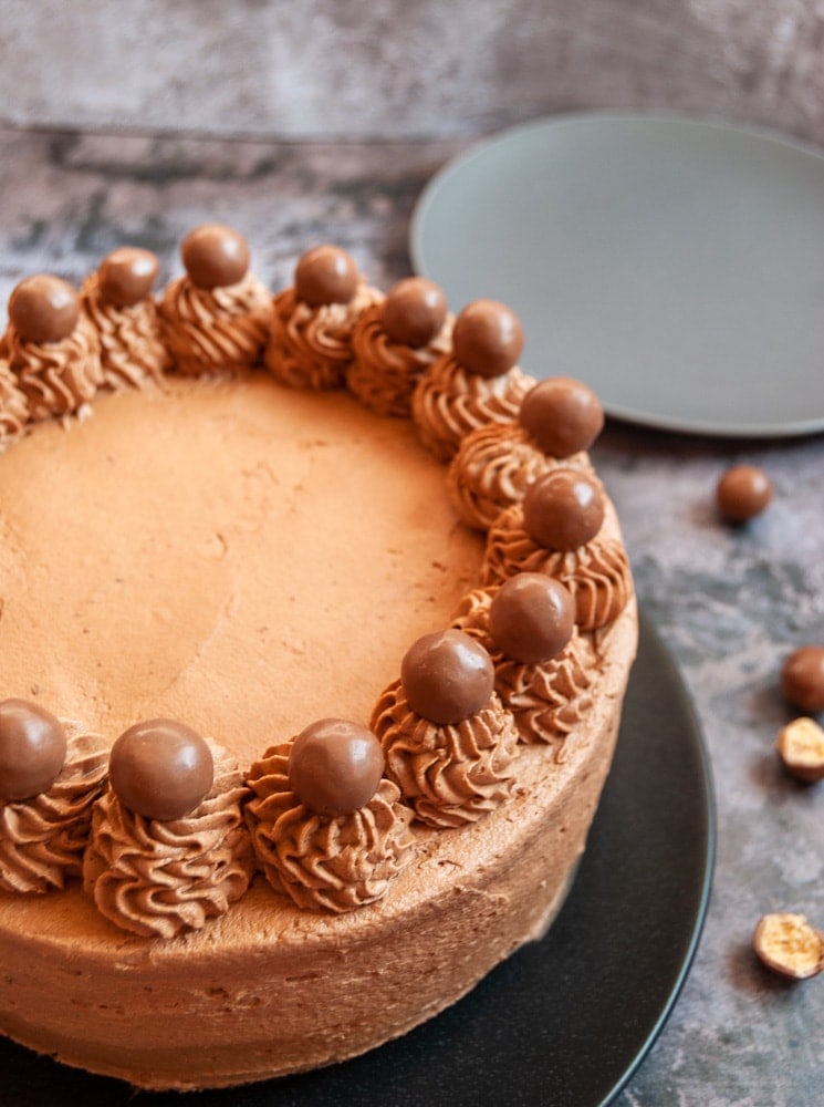 A chocolate cake decorated with piped chocolate fudge frosting and Maltesers on a black plate