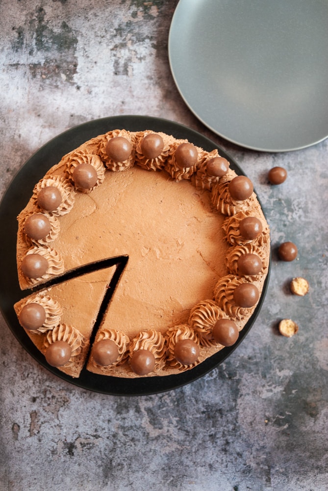 A chocolate cake with piped fudge frosting with a slice cut out of it.