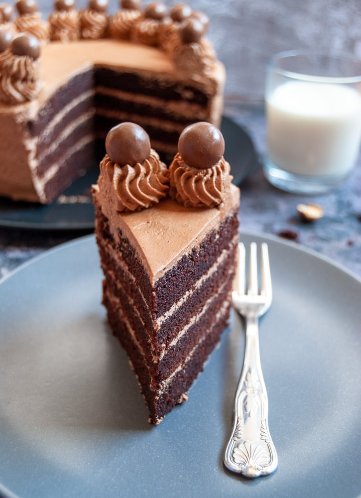 A close up photo of a cut piece of chocolate cake on a grey plate with a silver cake fork. 