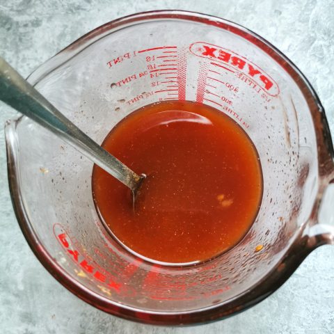A glass Pyrex jug of homemade sweet and sour sauce on a grey background