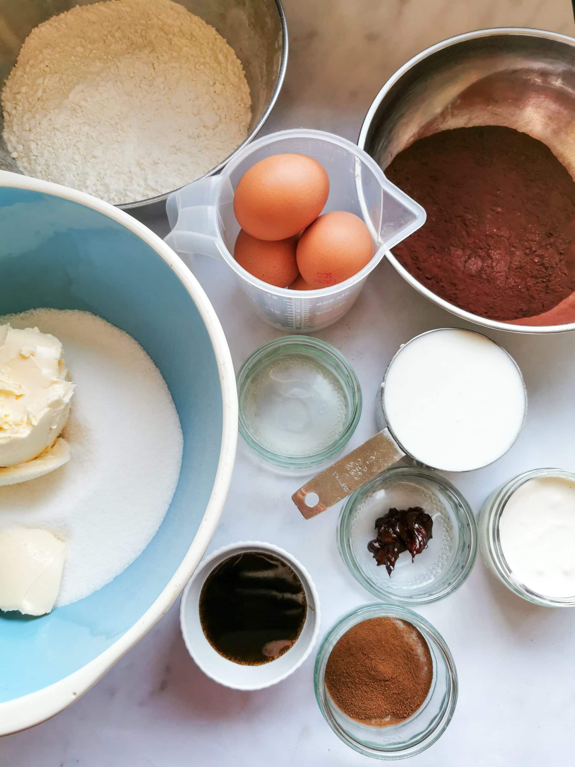 Eggs in a jug, butter and sugar in a large bowl and pots of cocoa powder, vanilla, buttermilk and red food colouring for making a red velvet cake