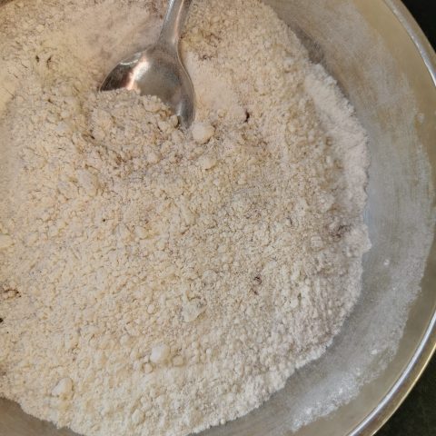 A silver bowl of flour with a spoon