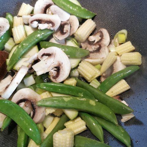 Stir fried snow peas, mushrooms and baby corn in a wok