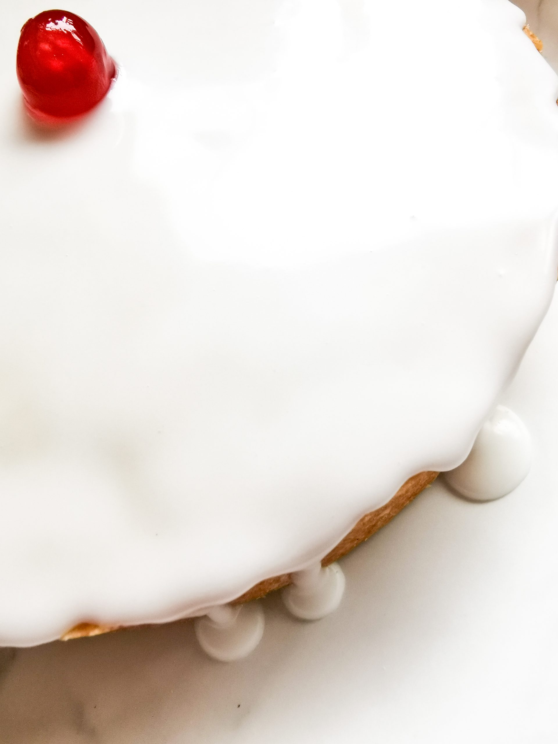 A large Empire biscuit topped with white icing and a red cherry on a white plate