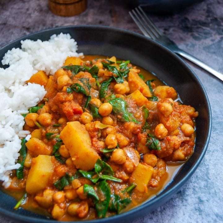 A stoneware bowl filled with chickpea, spinach and potato curry with boiled white rice.