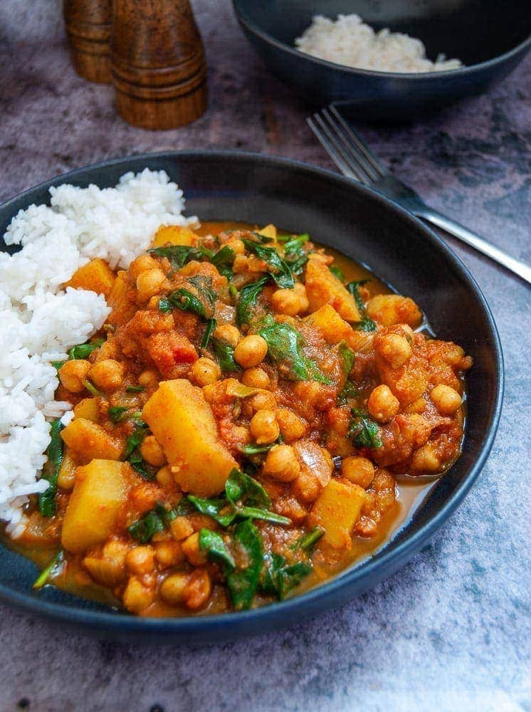 A stoneware bowl filled with chickpea, spinach and potato curry with boiled white rice.