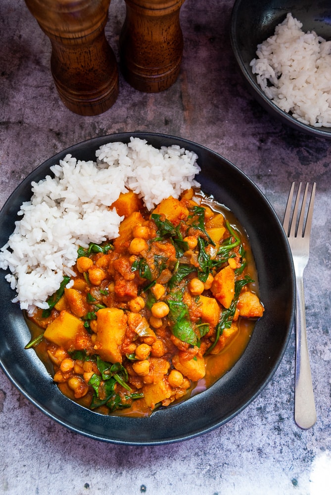 A bowl of chickpea and potato curry with white boiled rice.