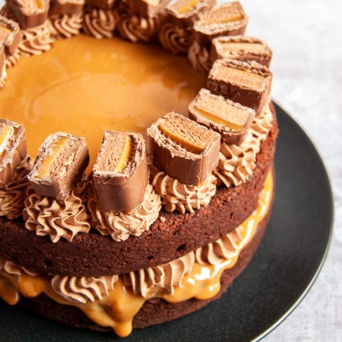 a chocolate cake on a black plate filled with oozing caramel and chocolate frosting, decorated with frosting and mars bars