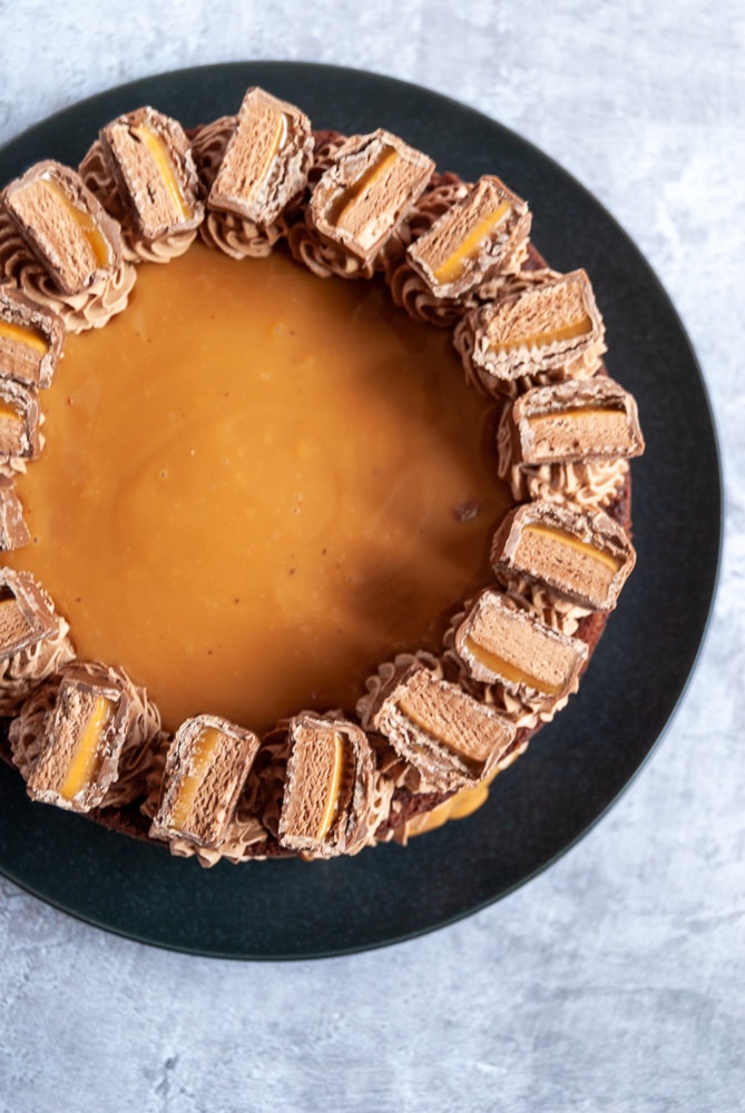 A flat lay photo of a chocolate cake covered in caramel sauce and decorated with mars bars