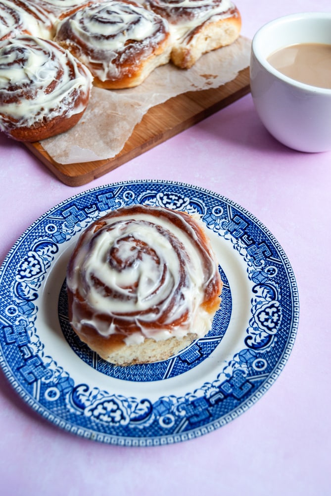 A cinnamon roll with cream cheese frosting on a blue willow pattern plate