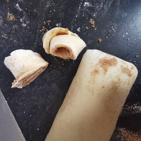 Cinnamon roll dough being cut into pieces