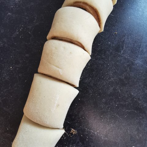 A row of unbaked cinnamon rolls on a dark work surface 