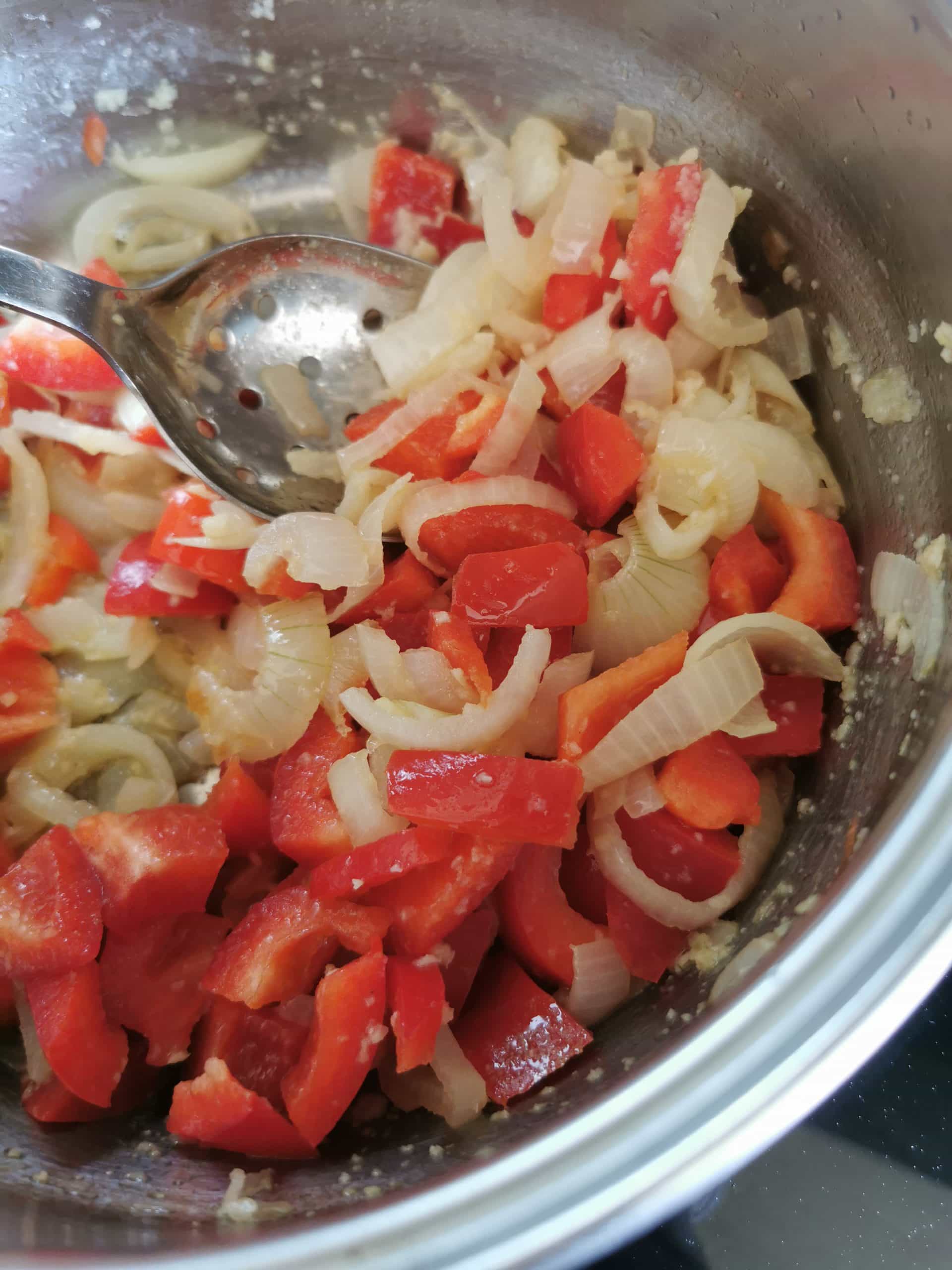 Onions, garlic, ginger and red bell peppers cooking in a frying pan 