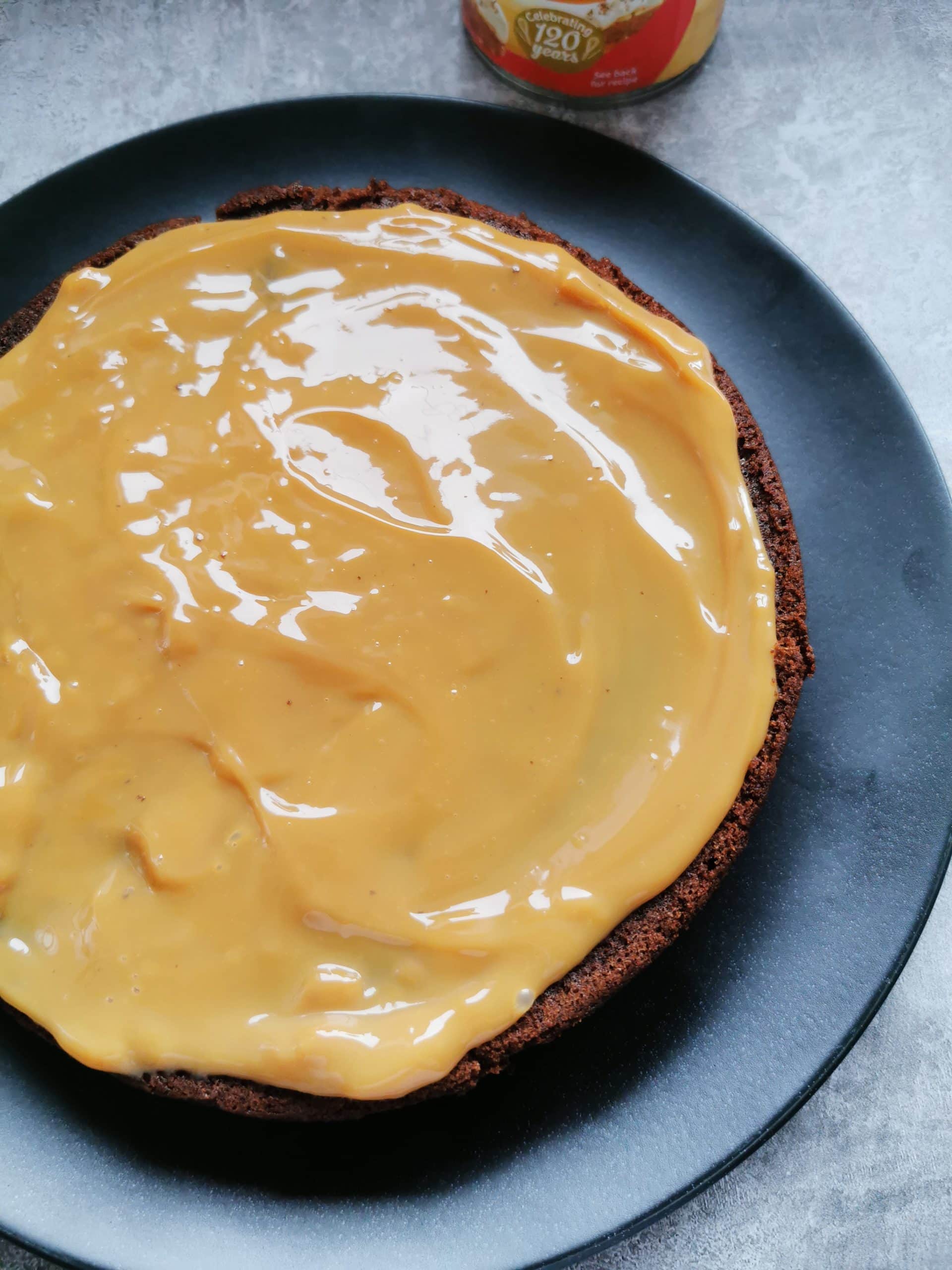 A chocolate cake on a black serving plate covered in caramel sauce.