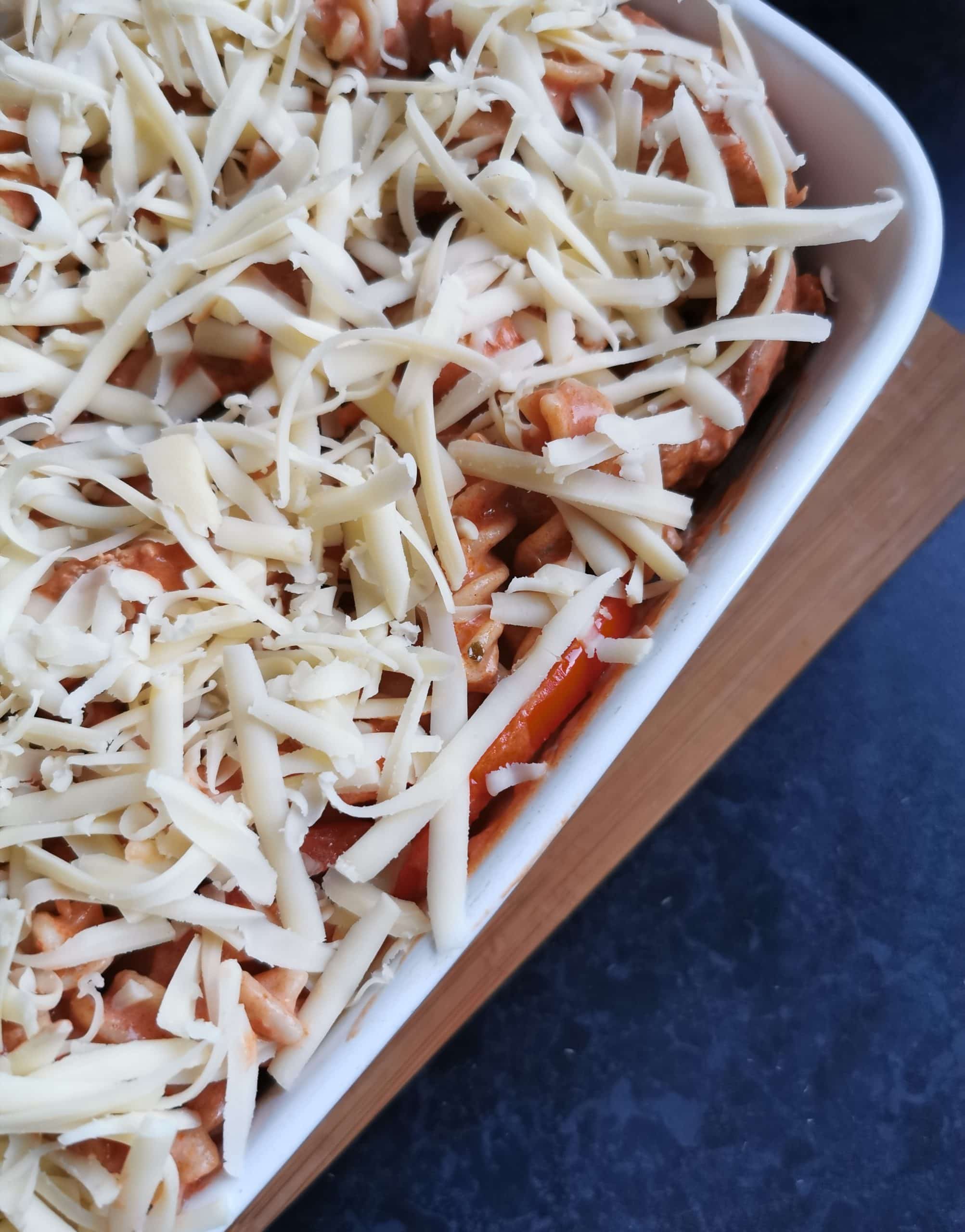 A white gratin dish of pasta coated in tomato sauce and covered in grated cheese