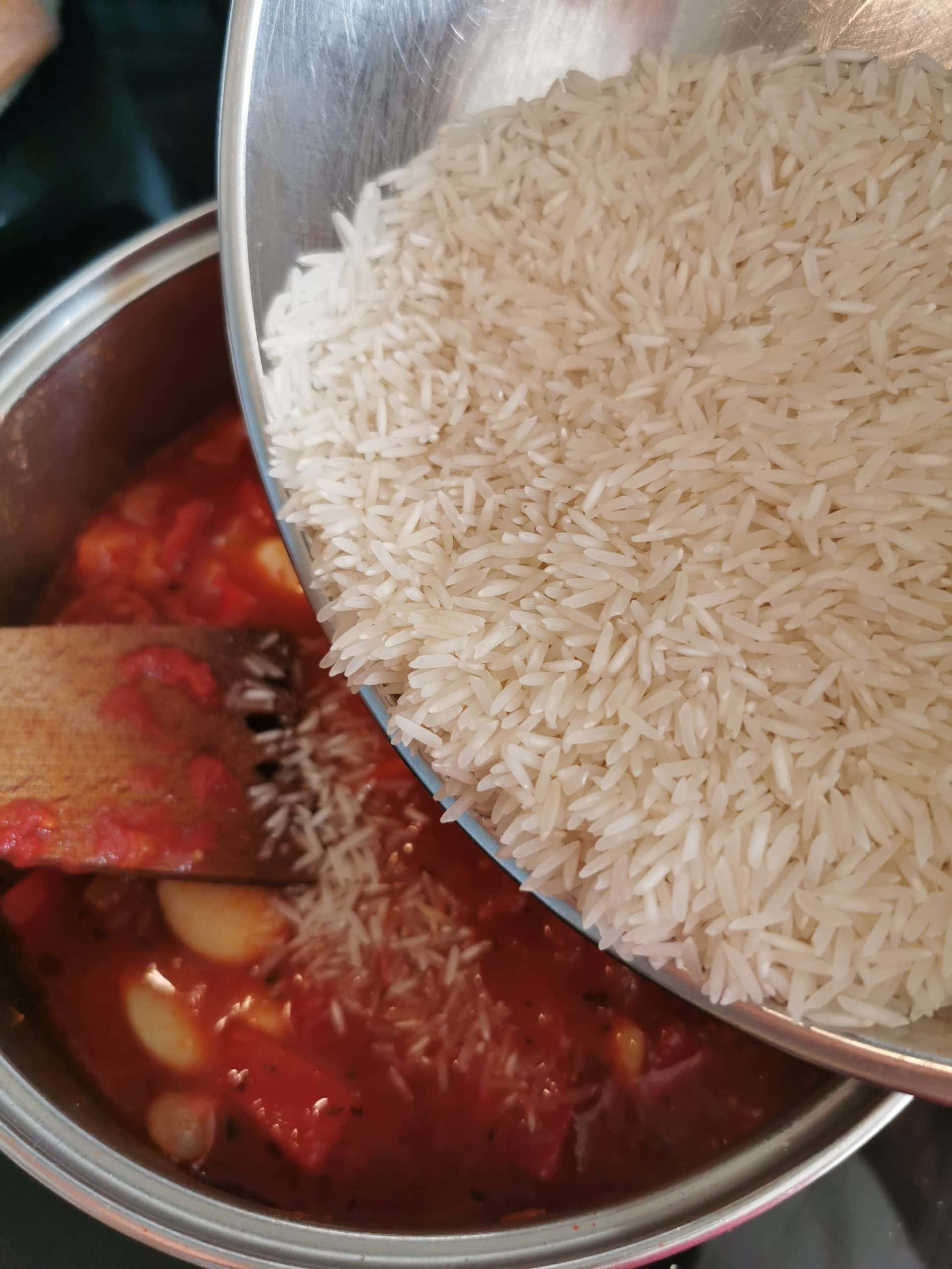 Rice being poured into a pan with chorizo, chopped tomatoes and peppers