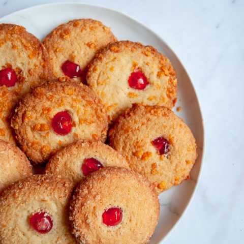 A plate of cornflake topped biscuits with a glace cherry in the middle