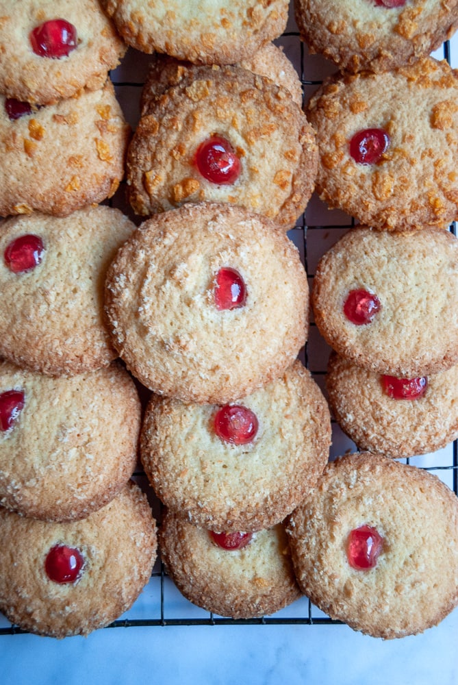 A wire rack of biscuits rolled in cornflakes and topped with a glace cherry