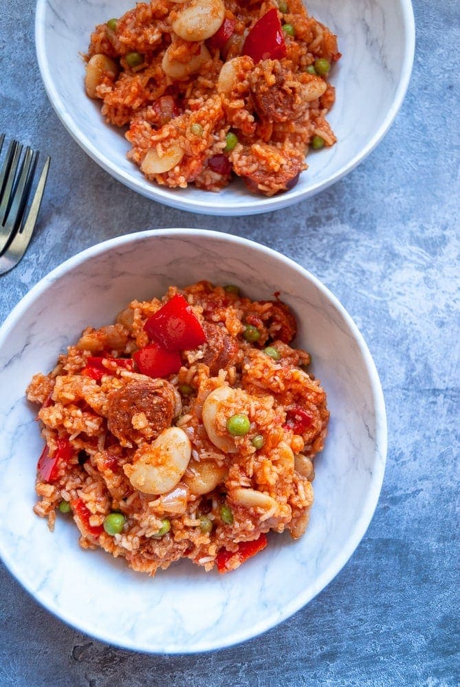 A flat lay photo of two bowls of one pot chorizo and pepper rice on a grey background 