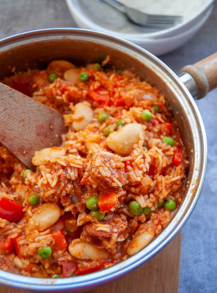 A pan of cooked rice with chorizo sausage, red peppers and peas 